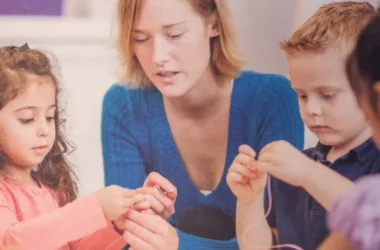 Eine Kindergärtnerin sitzt mit drei Kindern an einem Tisch und bastelt.